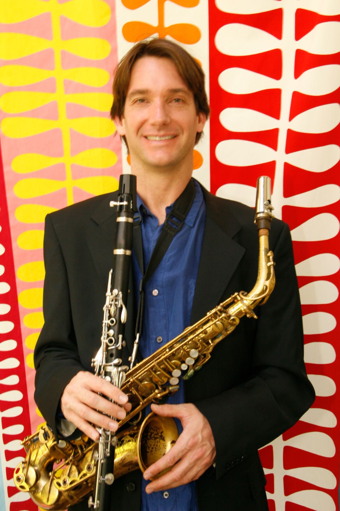 Dan holding clarinet and alto saxophone against a bold red and yellow backdrop